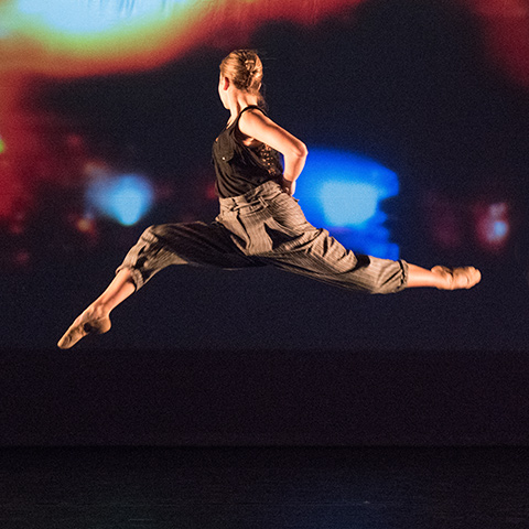 A dance student jumps in the air looking away from the audience  