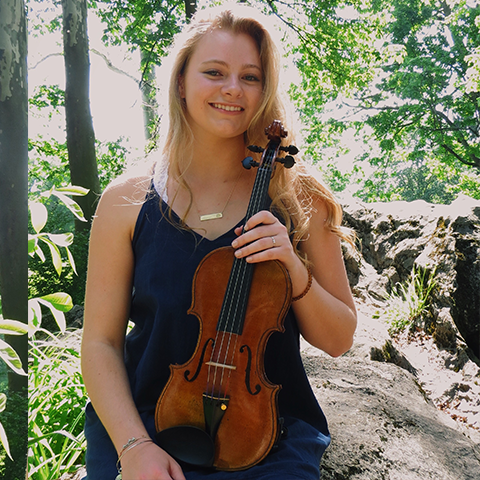 Student holding violin in forest