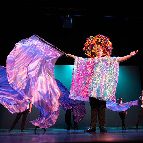 a dancer on stage with a purple and pink scarf