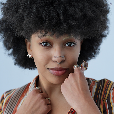 Naomi Wilcox headshot: grinning with hands resting on collarbone/cheek area