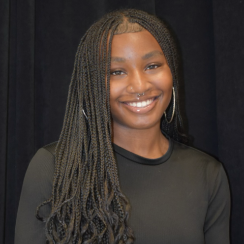 Zakiya Hudson headshot: smiling in a black shirt in front of a black background.