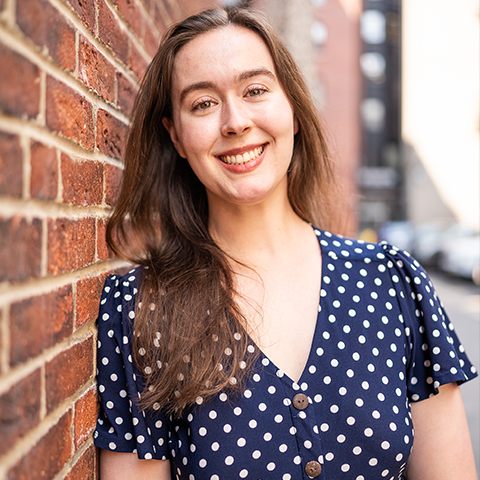 Kendall Floyd headshot: smiling in a polka dot top in front of a brick wall.