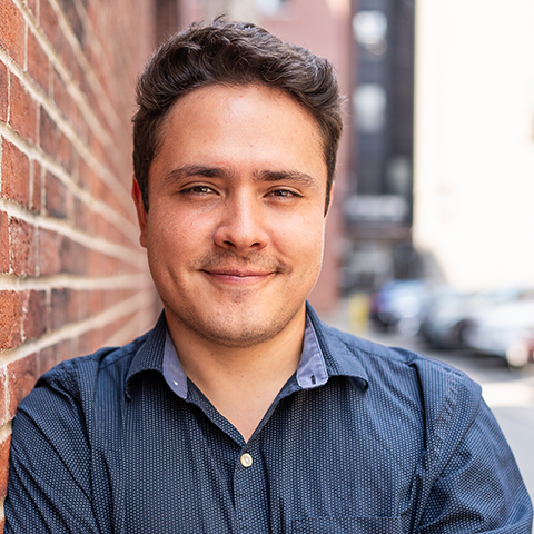 Luis Herrera grinning in front of a brick wall.