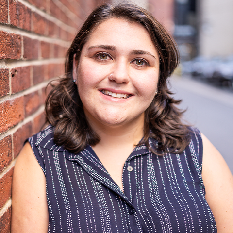 Taylor Kaufman headshot: smiling in a striped shirt in front of a brick wall