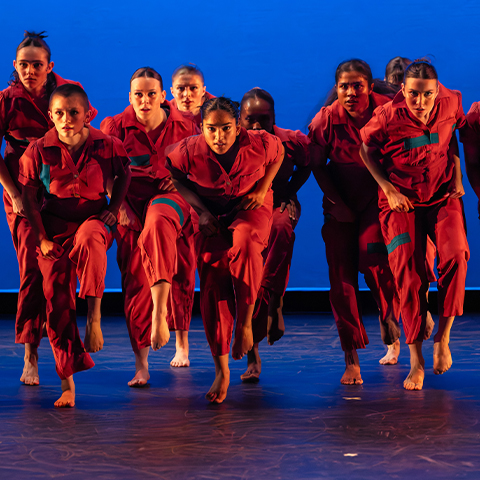 Dancers on stage, leaning forward in red outfits with a blue backdorp.