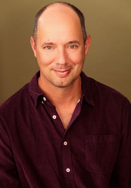 Headshot of Doug Lockwood wearing a maroon, button up in front of a brown background