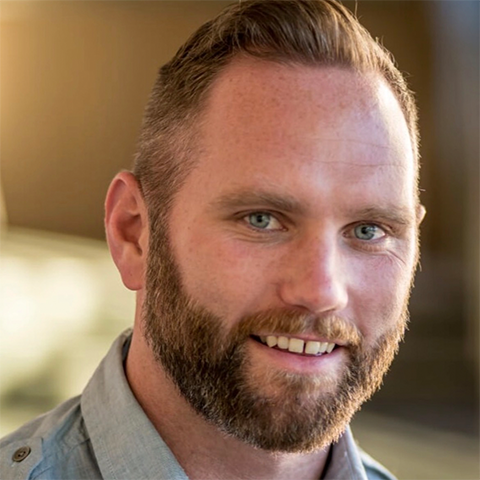 Andrew Houlihan headshot: smiling in front of a brown background in a collared shirt.