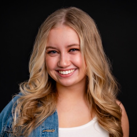 Emily Cosenza headshot: smiling in a denim jacket and white t-shirt in front of a black background