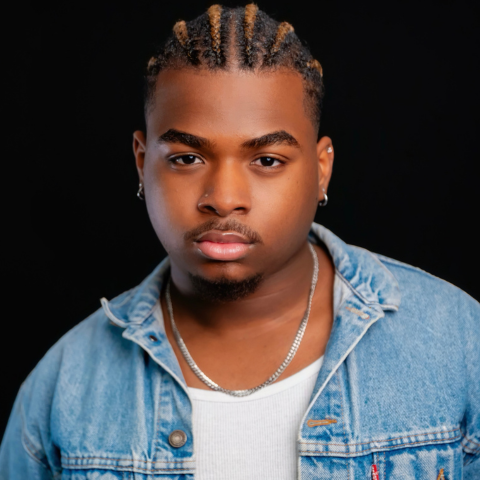Ray Aurelio headshot: wearing jean jacket and a white top in front of a black background