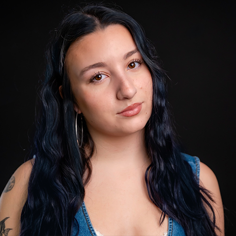 Ellie DeMeo headshot: wearing a denim top in front of a black background.