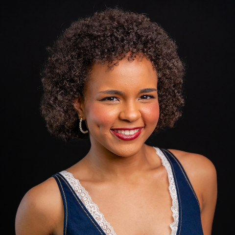 Olivia Reid headshot: wearing denim tank top in front of a black background