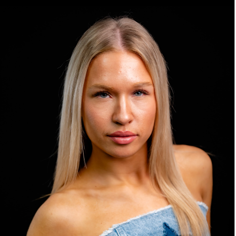 Oyla Pence headshot: wearing a strapless denim top in front of a black background.