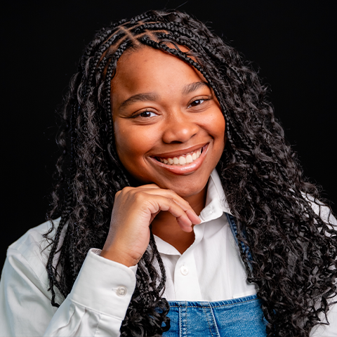 Rianne Thomas headshot: wearing a white button down under a denim top in front of a black background