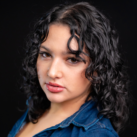 Sasha Plowman headshot: wearing a denim shirt in front of a black background.
