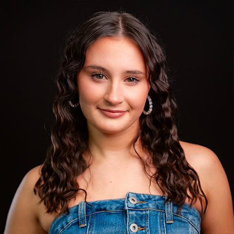 Katelyn Cote headshot: smiling in strapless denim top in front of a black background