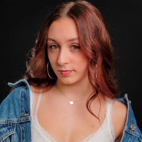 Brittany Dinapoli headshot: wearing a white shirt and denim jacket in front of a black background