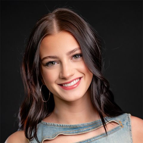 Ava Vannuccini headshot: smiling in a denim top in front of a black background.