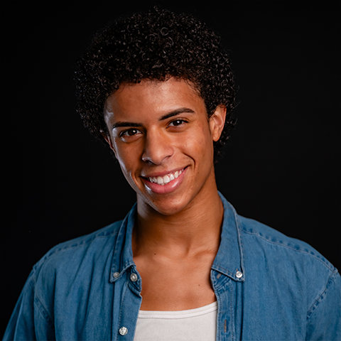Devin Glass headshot: smiling in a jean jacket and white shirt in front of a black background