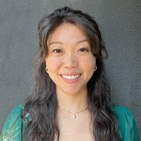 Moriah Tom headshot: grinning in a teal shirt in front of a gray background