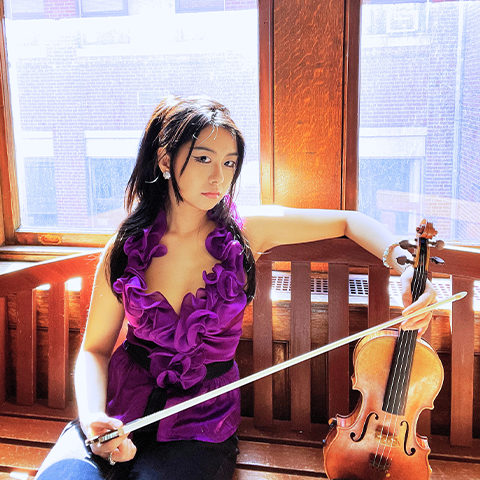 Photo of Jocelyn Wang in a purple shirt sitting on a bench posing with a violin