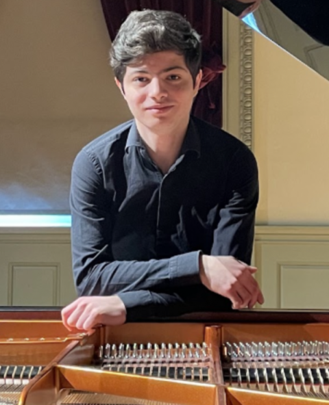 Tigran Mardanyan sitting in front of a piano in all black clothes