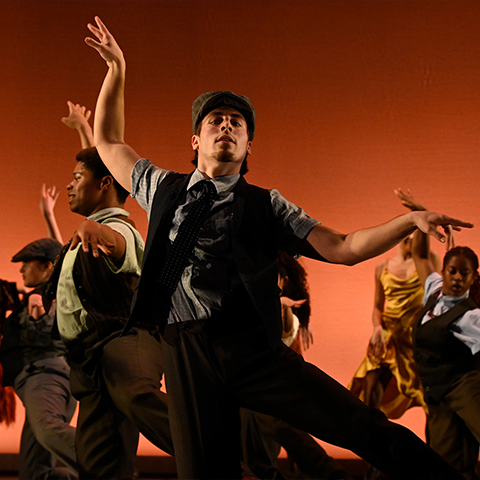 Dance students on stage with arms extended outwards in front of an orange background