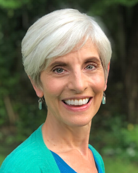 Andrea Southwick headshot: Andrea is smiling and wearing a teal sweater and dark blue shirt with trees in the background.