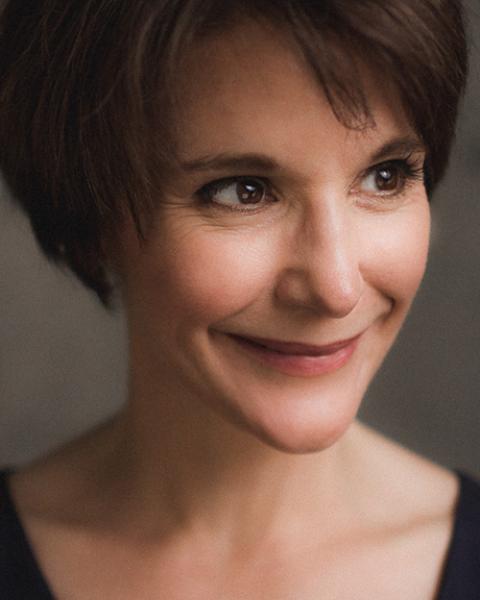 Wanda Strukus headshot: smiling with grey background wihle wearing a black u-length top.