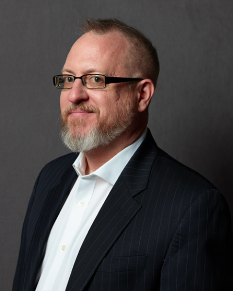 Andrew Bisantz smiling; wearing glasses in a black suit with a white undershirt