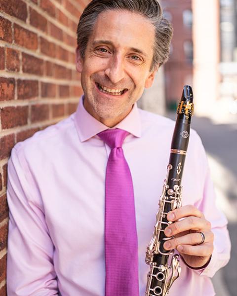 Matthew Marsit headshot, in pink shirt, pink tie, and holding clarinet.