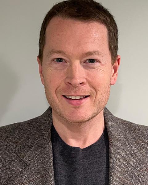 Andrew Shryock headshot; wearing black shirt with gray blazer in front of a white/gray background