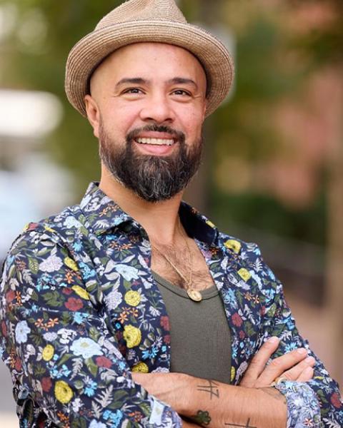 Nino De Los Reyes headshot: wearing a tan hat smiling with arms crossed