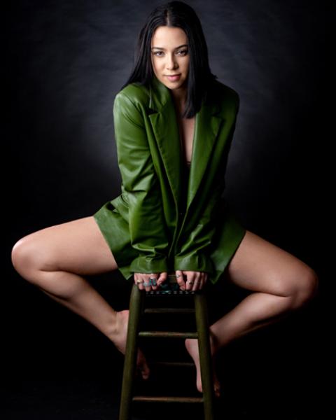 Alexis Beffer posing on a stool, wearing a green blazer.