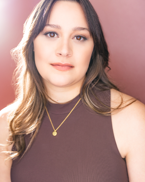 Holly Bourdon Faust headshot: grinning in front of a pale magenta wall in a mauve shirt.