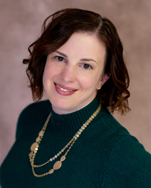 Megan Stahl headshot. Smiling in green shirt with gold chain.