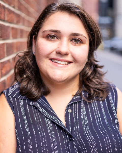 Taylor Kaufman headshot: smiling in a striped shirt in front of a brick wall