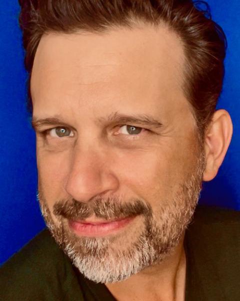 Brian Avers headshot: smiling in front of blue background.