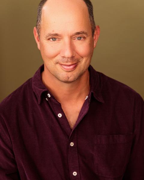 Headshot of Doug Lockwood wearing a maroon, button up in front of a brown background