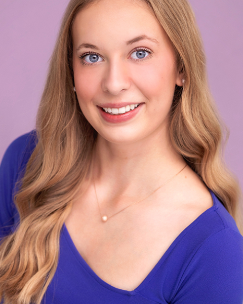 Tahlia Knoshaug headshot:s miling and wearing a blue shirt in front of a pink background