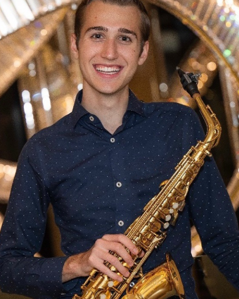 Xander Dawson headshot: smiling and holding a saxophone