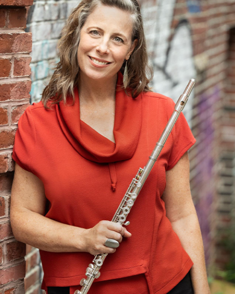 Sarah Brady headshot: wearing a red/orange shirt and holding her flute