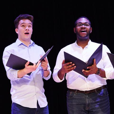 Two students sing together while holding sheet music