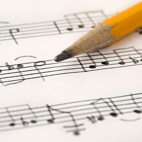 A pencil rests on top of handwritten sheet music