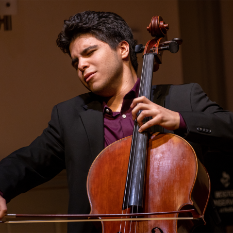 Andres Celis playing the cello with eyes closed in black shirt
