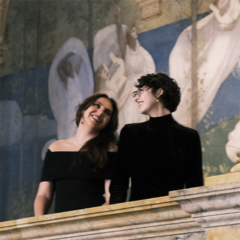 Two students in concert black clothing looking at each other in front of a religious mural