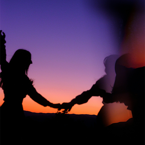 A silhouette of two people holding hands in front of a purple-orange sunset