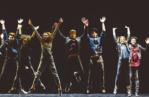 Musical theater students jump together on stage with hands in the air