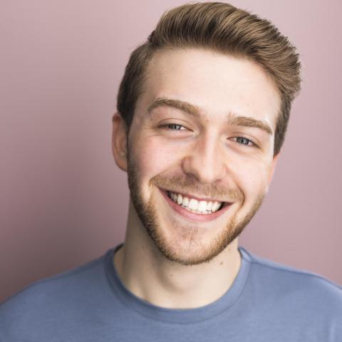 Ryan Norton headshot: smiling in blue shirt with pink background
