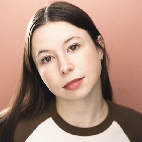 Alison Ragazzini headshot: posing in white and brown baseball t-shirt with pink background