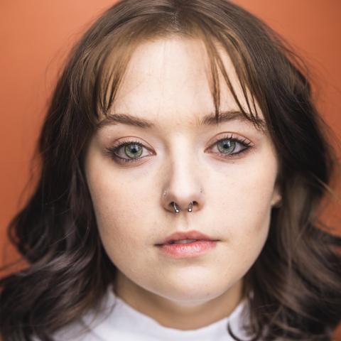 Kaitlyn Sumner headshot: posing in white shirt and burnt-orange background